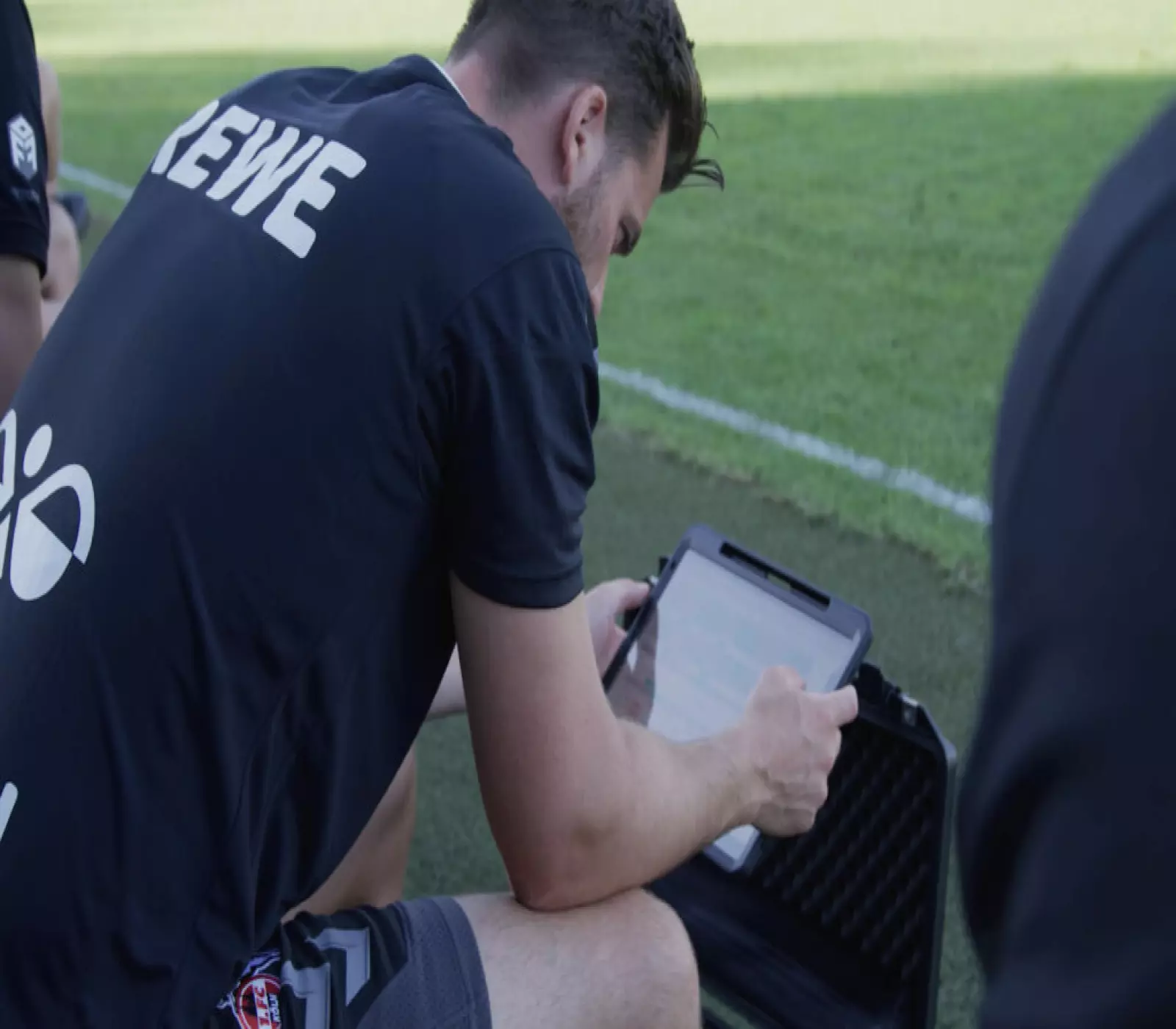 محلل رياضي يعمل على جهاز كمبيوتر محمول مزود ببرنامج لتحليل المباريات، ويطل على ملعب كرة قدم ممتلئ من مقصورة الصحافة.