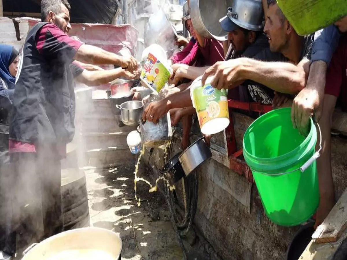 عاملون في مطبخ مجتمعي يسكبون شوربة العدس في أوعية النازحين بالقرب من الخيام المنصوبة في المناطق الغربية من مدينة غزة.