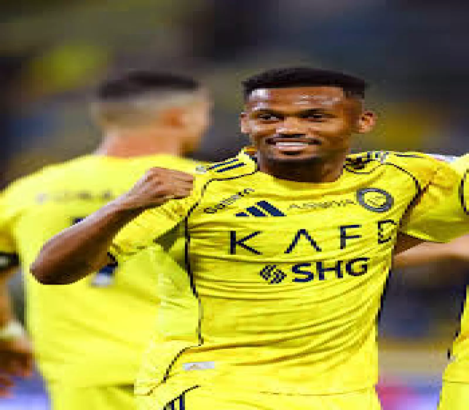 لاعب يرتدي قميص نادي النصر الأصفر يبتسم ويحتفل في الملعب رافعاً قبضة يده.