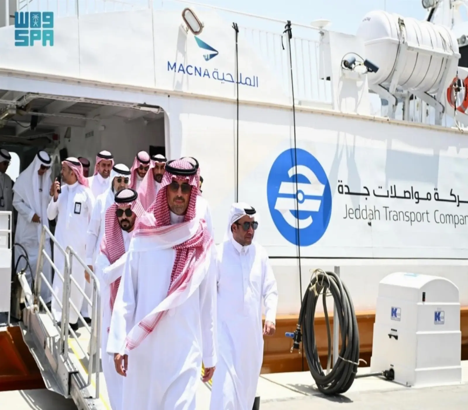 مجموعة من الرجال يرتدون الزي السعودي التقليدي يغادرون عبارة تابعة لشركة مواصلات جدة عبر جسر مشاة.